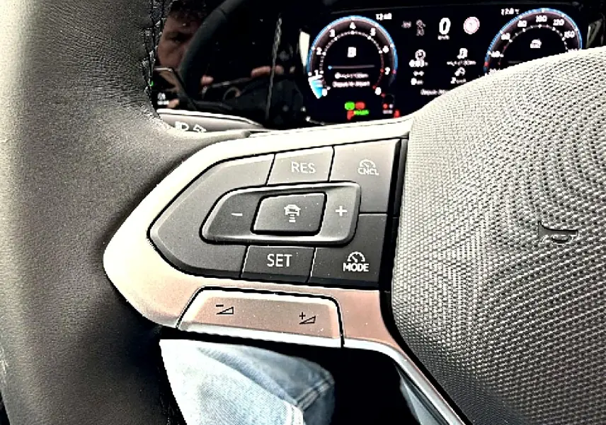 Gros plan sur le volant noir de la Volkswagen Golf 2026, avec commandes intégrées et tableau de bord numérique en arrière-plan.