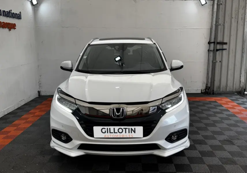Vue avant d'un Honda HR-V blanc 2019 avec calandre chromée et feux LED allumés dans un showroom.
