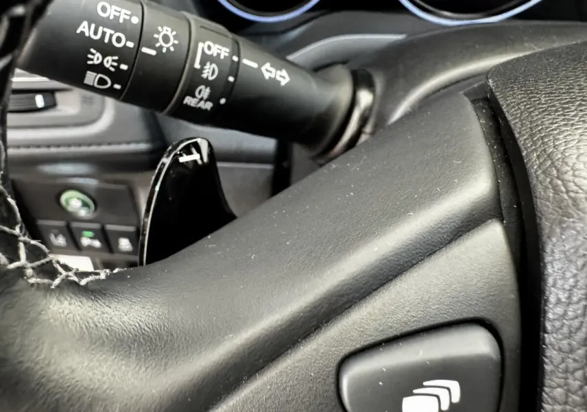 Gros plan sur le volant noir et la commande des phares du tableau de bord du Honda HR-V 1.5 i-VTEC 130 Exclusive 2019.