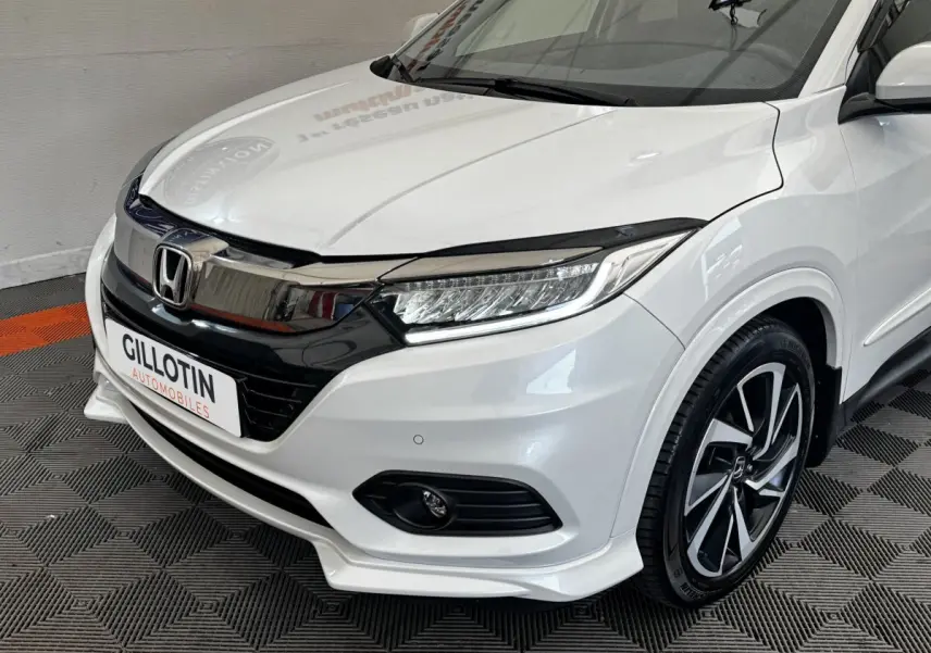 Vue 3/4 avant droit d'un Honda HR-V blanc 2019 avec calandre chromée et jantes alliage noires et argentées.