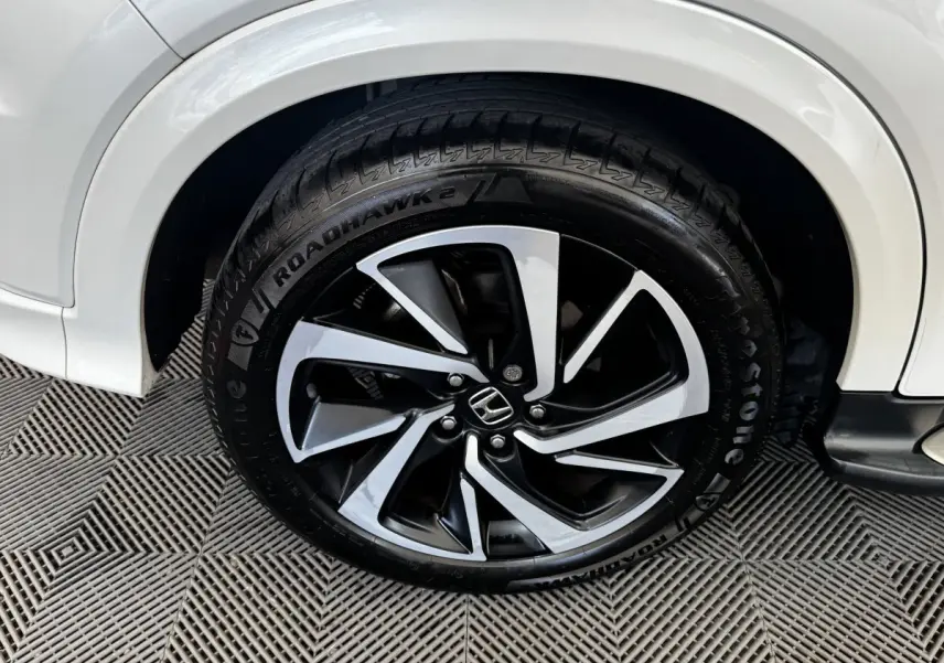 Gros plan sur la roue avant droite d’un Honda HR-V blanc, jante alliage noire et argentée avec logo Honda central.