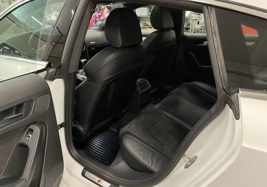 Vue intérieure arrière côté gauche d'une Audi A5 Sportback blanche de 2015 avec sièges noirs en cuir et alcantara.