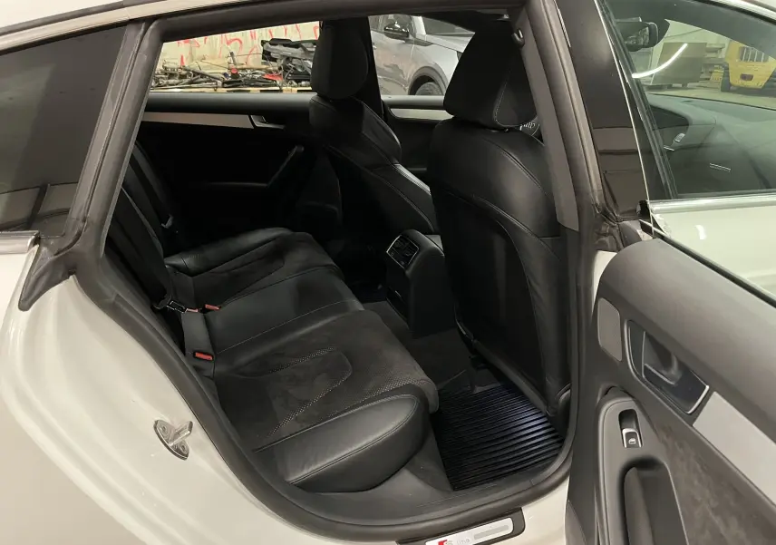 Vue intérieure arrière côté gauche d'une Audi A5 Sportback blanche avec sièges noirs en cuir et alcantara, finition S line.