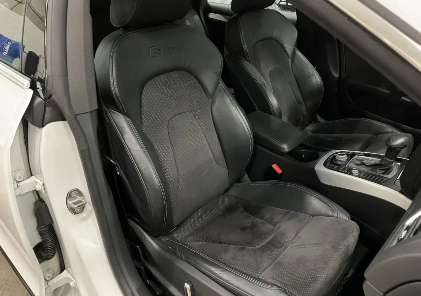 Vue intérieure côté conducteur de l'Audi A5 Sportback blanche, sièges sport S line en cuir noir avec console centrale visible.