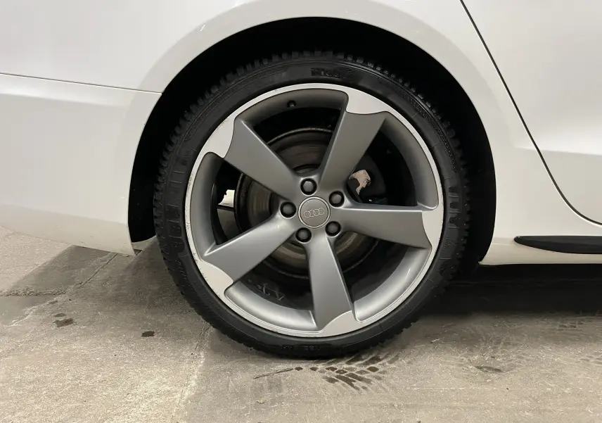 Gros plan sur la roue arrière droite de l'Audi A5 Sportback blanche avec jante alliage grise à cinq branches.