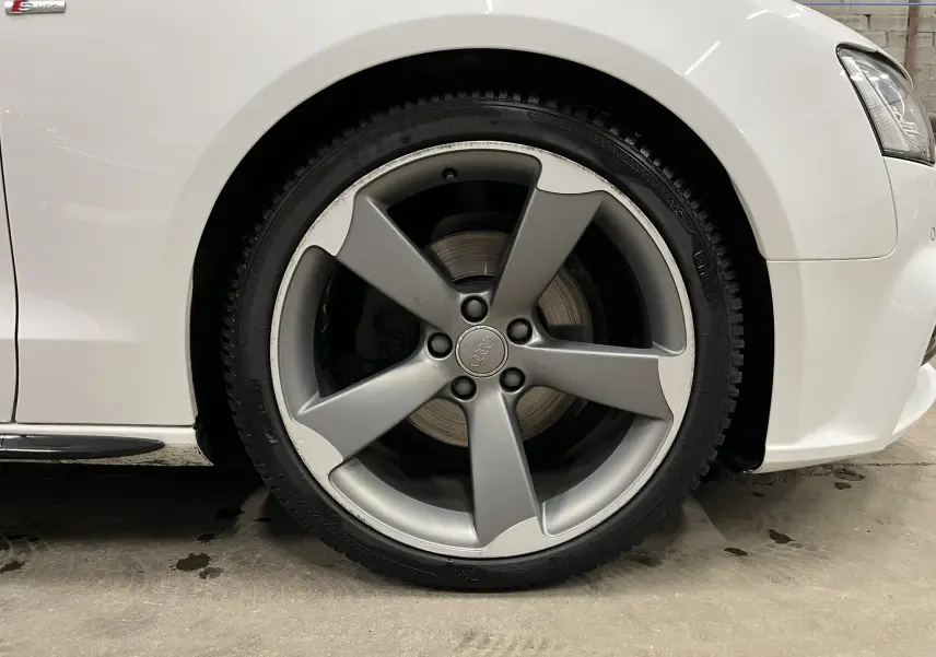 Gros plan sur la roue avant droite de l'Audi A5 Sportback blanche avec jante alliage cinq branches et logo Audi au centre.