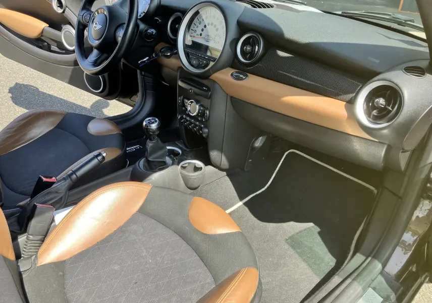 Intérieur avant droit d'une MINI Cooper S R56 2012 marron, sièges bi-ton cuir et tissu, tableau de bord noir et marron.