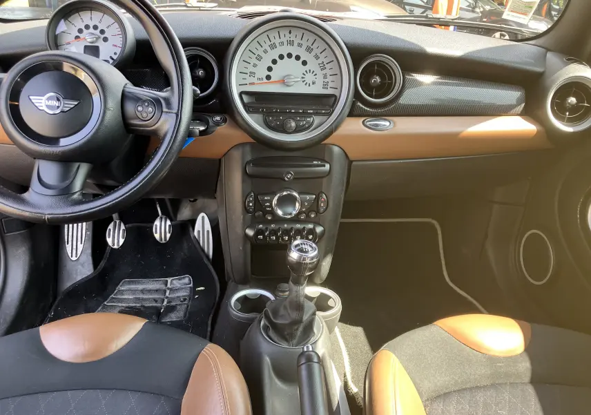 Vue intérieure avant de la MINI Cooper S R56 2012, avec tableau de bord marron et noir, volant multifonction et boîte manuelle.
