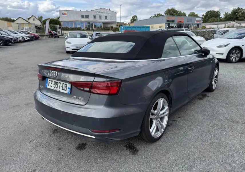 Audi A3 Cabriolet gris vue 3/4 arrière droit avec capote noire en position fermée sur parking extérieur.