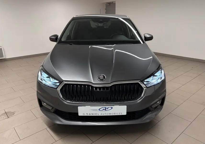Vue avant d'une Skoda Fabia 2023 gris graphite métallisé avec phares allumés dans un showroom.