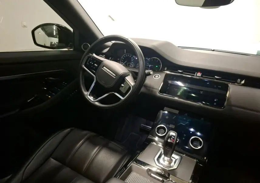 Vue intérieure côté conducteur du Range Rover Evoque 2022, avec volant cuir perforé et écran tactile central noir.