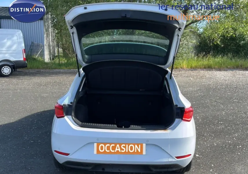 Vue arrière d'une SEAT LEON blanc neige 2025 avec le coffre ouvert sur un parking extérieur.