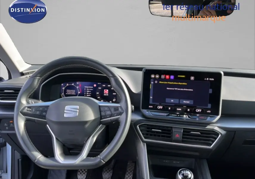 Vue intérieure frontale du tableau de bord de la SEAT LEON blanc neige 2025 avec volant multifonction et écran tactile central.