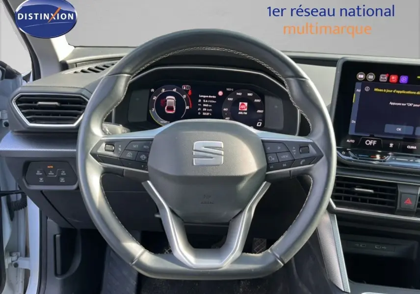 Vue rapprochée du volant et du tableau de bord numérique d’un SEAT Leon blanc neige 2025, intérieur moderne.