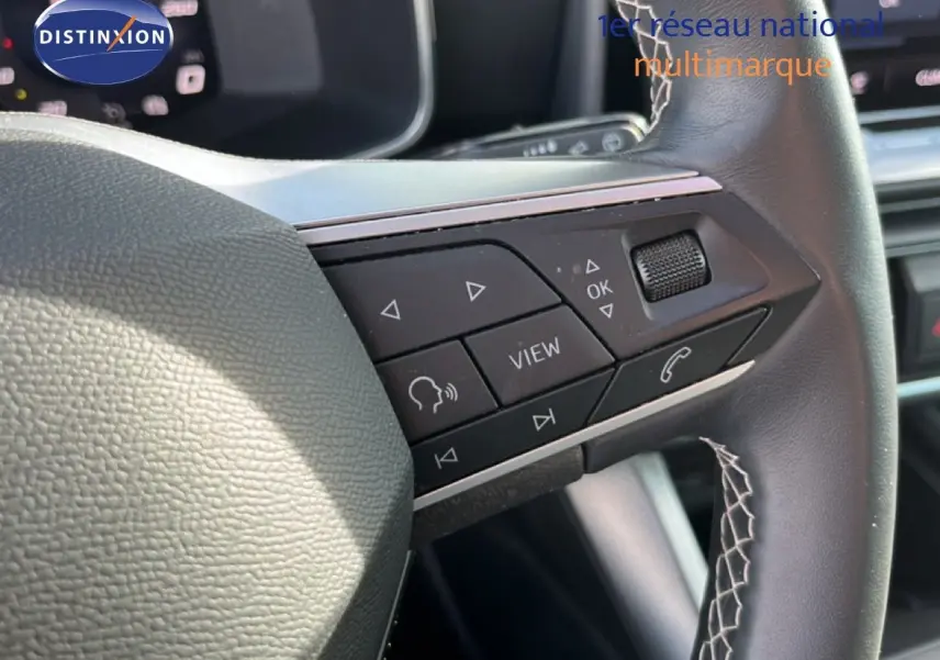 Gros plan sur les commandes multifonctions à droite du volant en cuir noir du SEAT Leon blanc neige 2025.