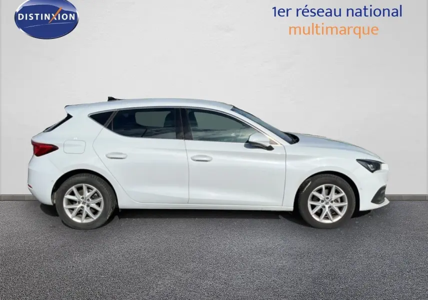 Vue de profil côté gauche d'une SEAT Leon blanc neige, compacte cinq portes avec jantes alliage et lignes épurées.