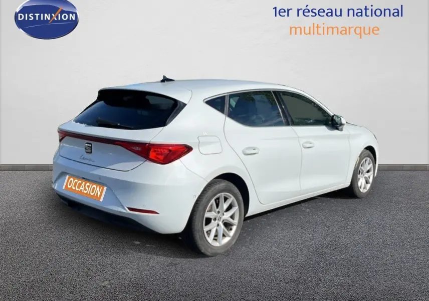 Vue 3/4 arrière droite d'une SEAT Leon blanche neige avec feux arrière LED et jantes alliage, stationnée sur sol gris.
