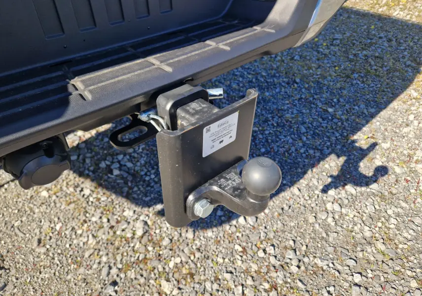 Gros plan sur l'attelage arrière noir du Ford Ranger Super Cabine gris Iconic, avec prise électrique visible, sur sol gravillonné.