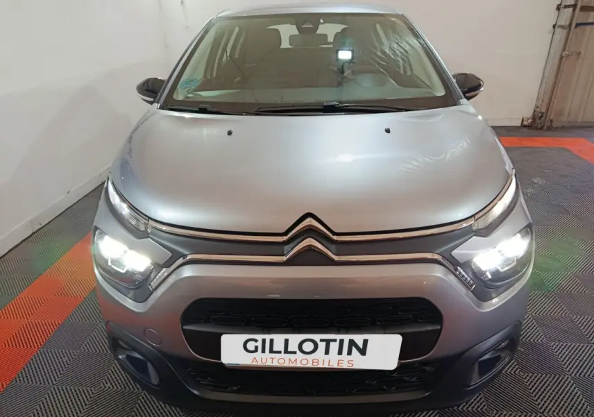 Vue frontale d'une Citroën C3 gris clair 2024 avec phares LED allumés dans un garage fermé.