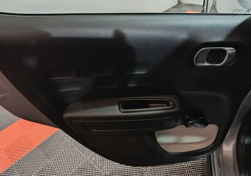 Vue rapprochée de la porte arrière droite intérieure noire d'une Citroën C3 gris clair 2024, avec poignée et manivelle de vitre.