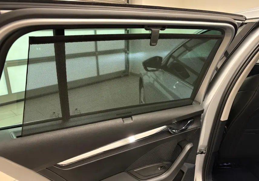 Vue intérieure de la porte arrière droite d'une Skoda Octavia Combi gris argent 2023 avec pare-soleil en filet déployé.