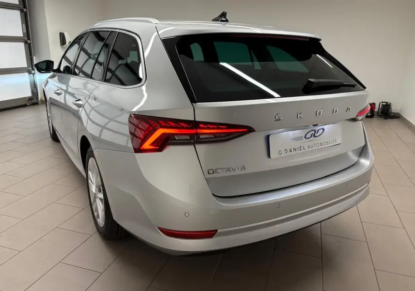Vue 3/4 arrière droite d'une Skoda Octavia Combi gris argent 2023 avec feux arrière LED allumés en intérieur showroom.