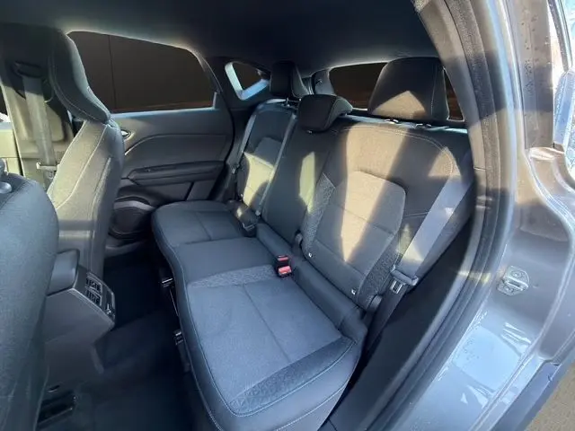 Vue intérieure arrière côté droit du Renault Captur 2024 gris Cassiopée, sièges tissu noir avec ceintures et appuie-têtes visibles.