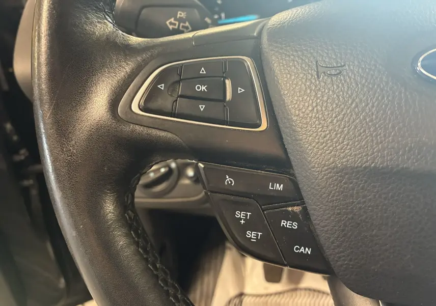 Gros plan sur le volant noir en cuir du Ford C-MAX gris, montrant les commandes de régulateur de vitesse et de navigation.