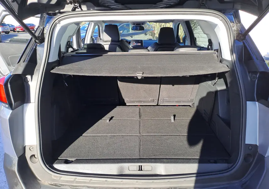 Coffre ouvert vu de l'arrière d'un Peugeot 5008 gris 2019, montrant l'espace de chargement avec cache-bagages déployé.
