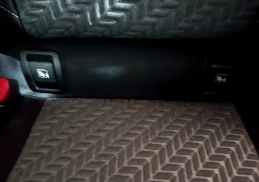 Détail du coffre de la Renault Clio Business blanc, montrant les commandes d'ouverture des sièges arrière et le tapis à motif chevrons.