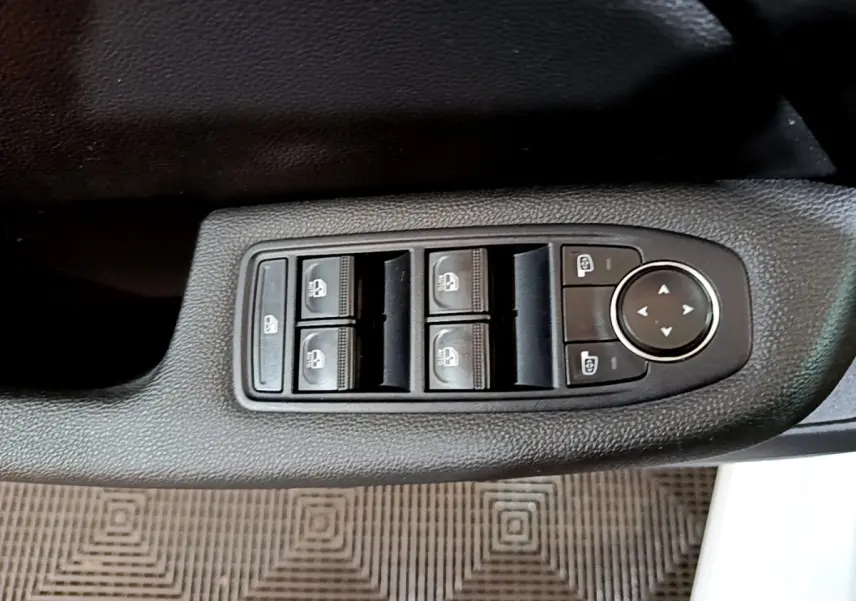 Gros plan sur les commandes des vitres électriques et rétroviseurs côté conducteur d’une Renault Clio blanche 2023.