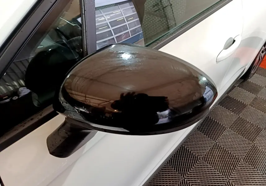 Rétroviseur noir en gros plan côté gauche sur Renault Clio Business blanc vue partielle du véhicule stationné.