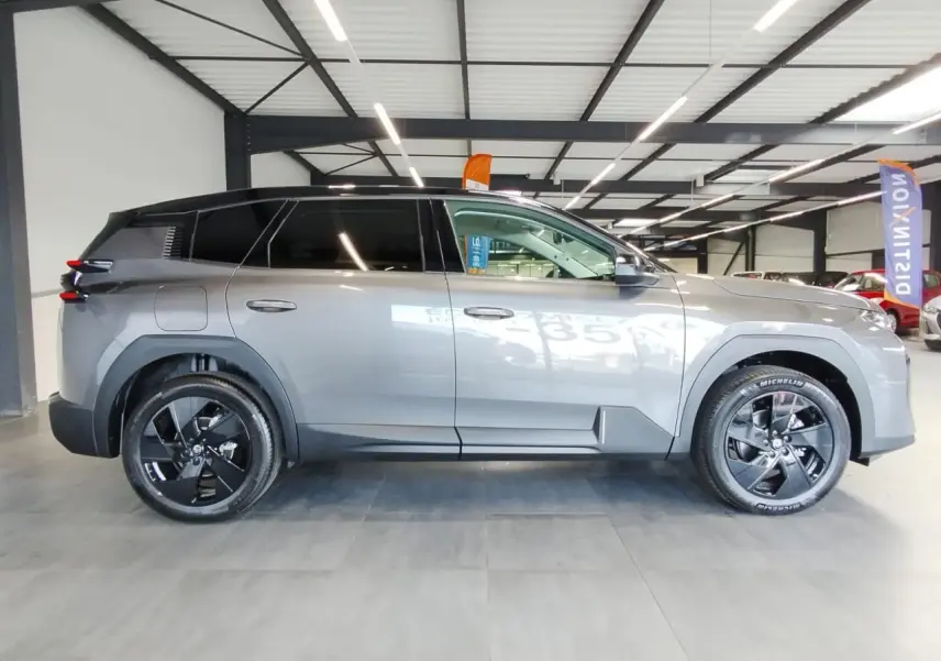 Profil côté gauche du Citroën C5 Aircross gris métallisé avec toit noir et jantes alliage noires en intérieur showroom.