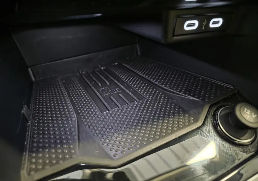 Gros plan sur le compartiment de rangement avant du Volkswagen T-Roc gris, avec ports USB-C et prise 12V visibles.