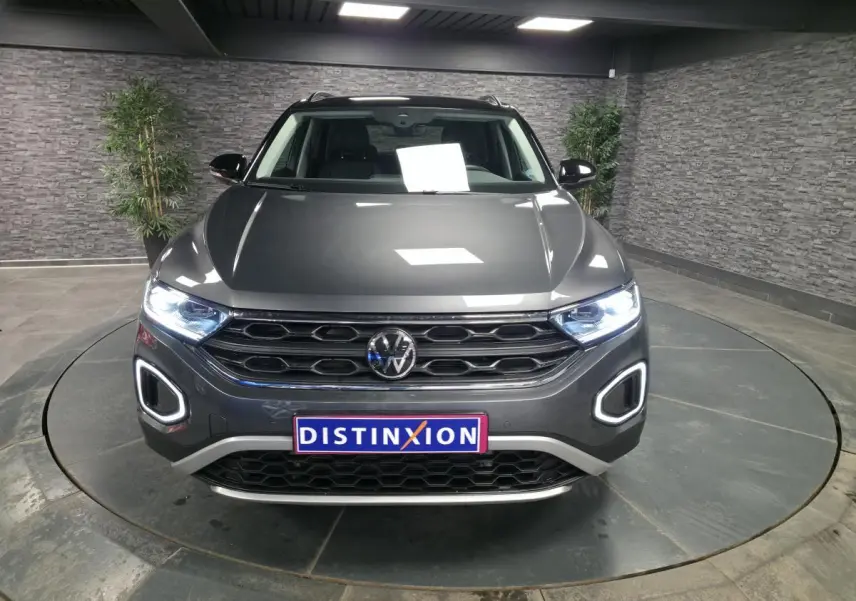 Vue de face d'un Volkswagen T-Roc gris métallisé avec feux LED allumés et calandre noire en showroom.