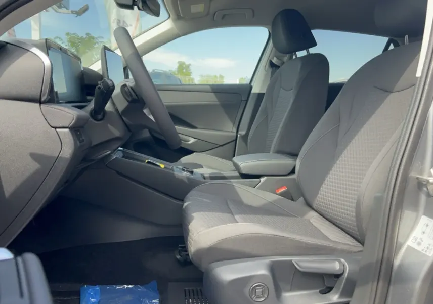 Vue intérieure côté conducteur du Volkswagen T-Roc gris loup 2026, sièges tissu et accoudoir central visibles.
