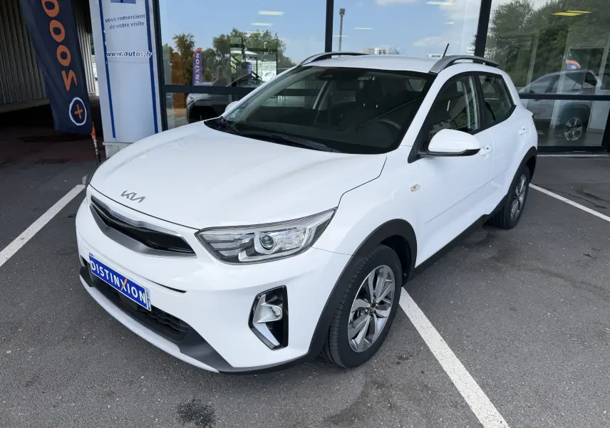 KIA Stonic blanc vue 3/4 avant droit, avec calandre noire et jantes alliage bicolores, stationné devant un bâtiment.