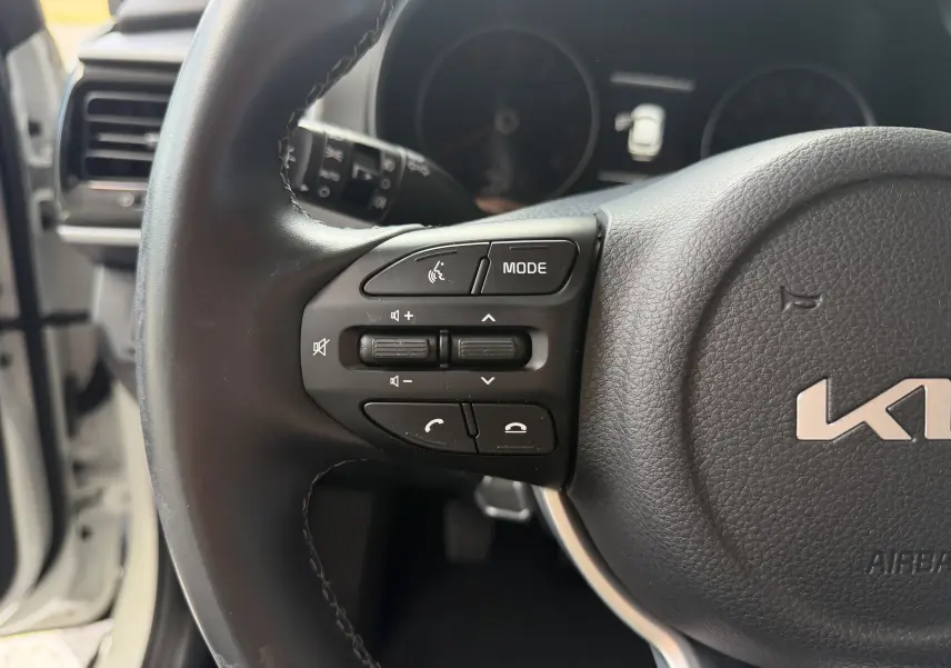 Gros plan sur le volant noir de la KIA Stonic blanc, avec commandes audio et téléphone côté gauche visibles.
