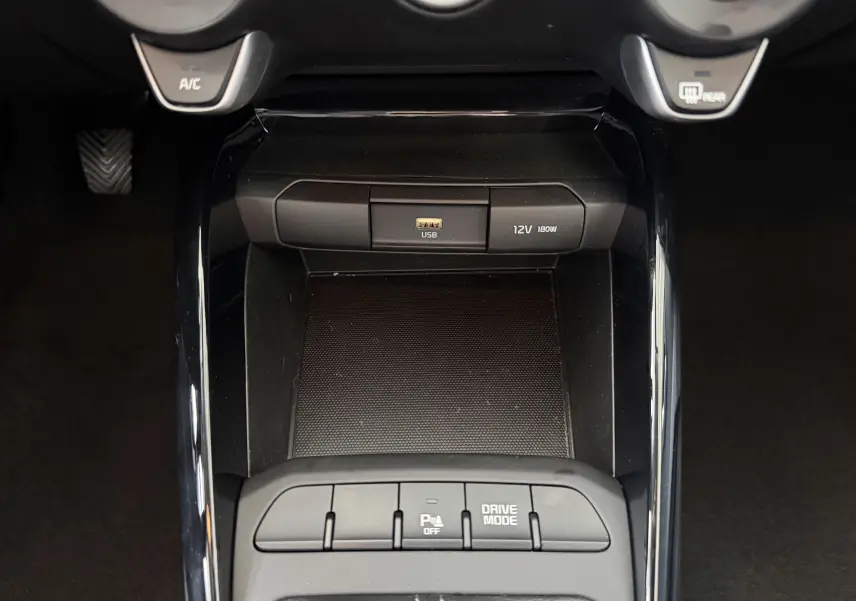 Vue rapprochée de la console centrale noire du Kia Stonic 2022, avec port USB, prise 12V et boutons Drive Mode.