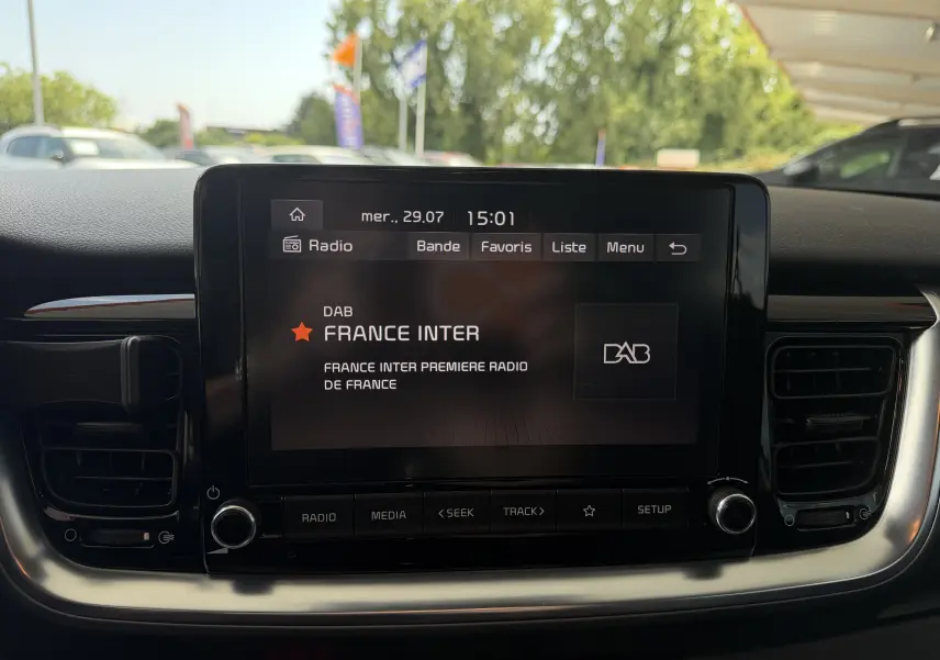 Écran tactile central du tableau de bord du KIA Stonic blanc, affichant la radio France Inter en extérieur jour.