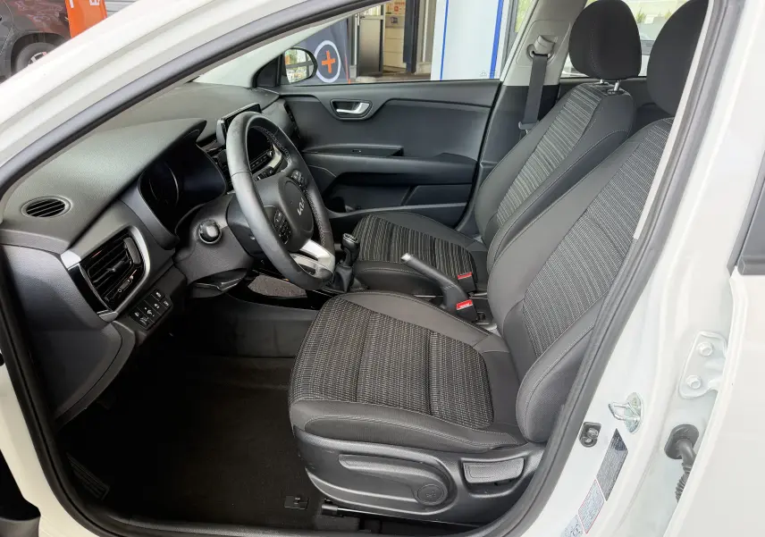 Vue intérieure côté conducteur du Kia Stonic blanc 2022, montrant sièges tissu noirs et tableau de bord moderne.
