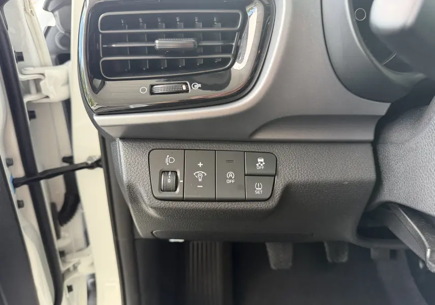Vue rapprochée côté gauche du tableau de bord blanc KIA Stonic 2022, montrant les commandes d’éclairage et d’assistance.