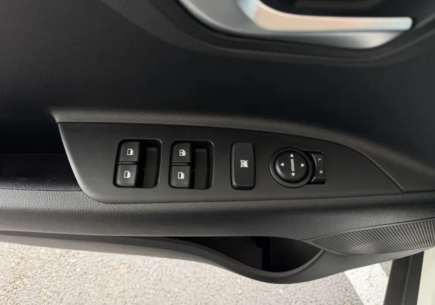 Vue rapprochée des commandes de lève-vitres et réglage des rétroviseurs sur la porte côté conducteur d'un KIA Stonic blanc.