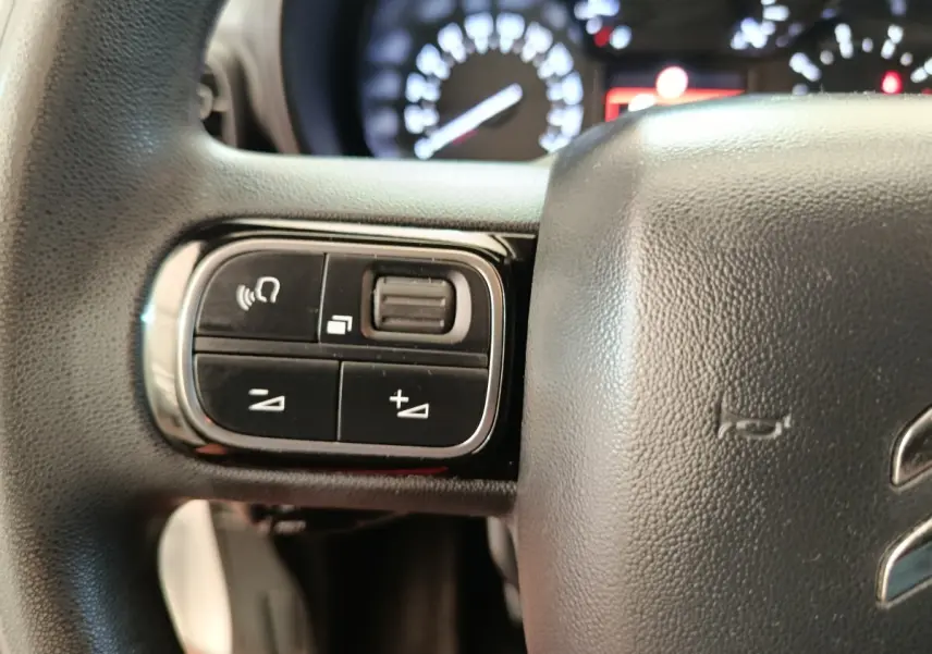 Gros plan sur les commandes gauche du volant noir du Citroën Berlingo 2020, avec tableau de bord flou en arrière-plan.