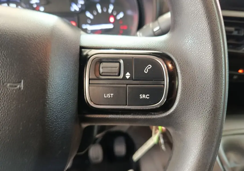 Gros plan sur les commandes gauche du volant noir du Citroën Berlingo blanc, avec tableau de bord flou en arrière-plan.