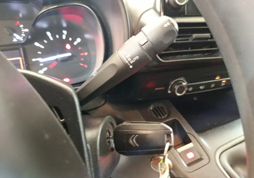 Gros plan intérieur sur le volant et le tableau de bord noir du Citroën Berlingo blanc, clé insérée dans le contact.