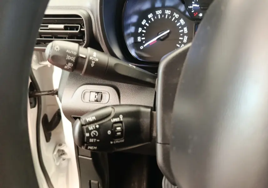 Gros plan sur le volant multifonctions et les commandes de régulateur de vitesse du Citroën Berlingo blanc, tableau de bord visible.