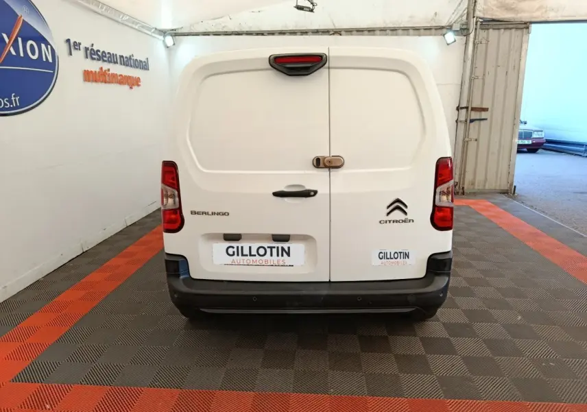 Vue arrière d'un utilitaire Citroën Berlingo blanc avec portes battantes et feux arrière rouges, stationné en intérieur.