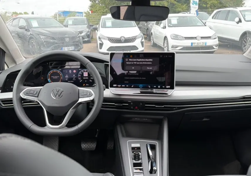 Vue intérieure de face du tableau de bord et volant noir d’une Volkswagen Golf 2026 avec écran tactile central et cockpit numérique.