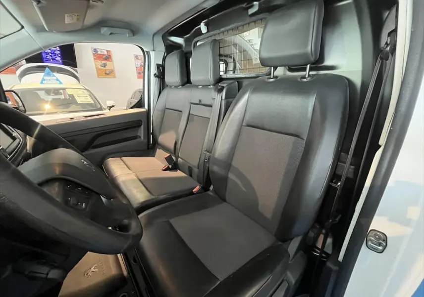 Intérieur du Peugeot Expert Fourgon 2019, vue côté conducteur montrant les sièges noirs et la cloison métallique blanche.